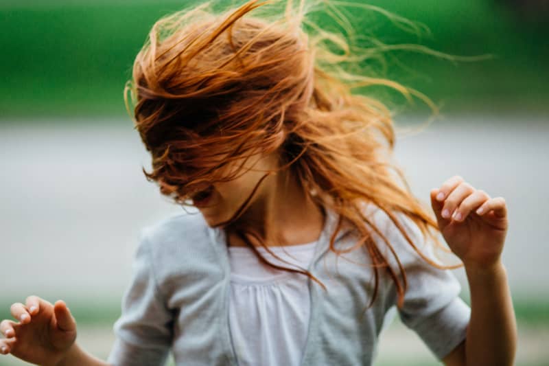 A girl's hair is blown across her face by wind.