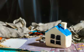 Miniature toy house stand on burnt money Euro bill banknotes.close up.Blurred long exposure background and foreground.Indoors shot.