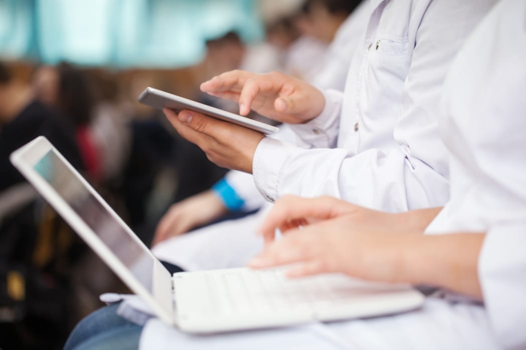 Male and female medical students or doctors using digital tablet and laptop during the lecture or conference. Focus on the man with pad