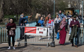 LONDON, UNITED KINGDOM - MARCH 30, 2021: People walk past a social distancing banner during exceptionally warm and sunny weather in St James's Park, making the most of eased Coronavirus restrictions, on 30 March, 2021 in London, England.