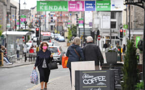 Members of the public, some wearing face coverings due to Covid-19, walk past shops in Kendal in Cumbria, north west England on 21 June 2021.