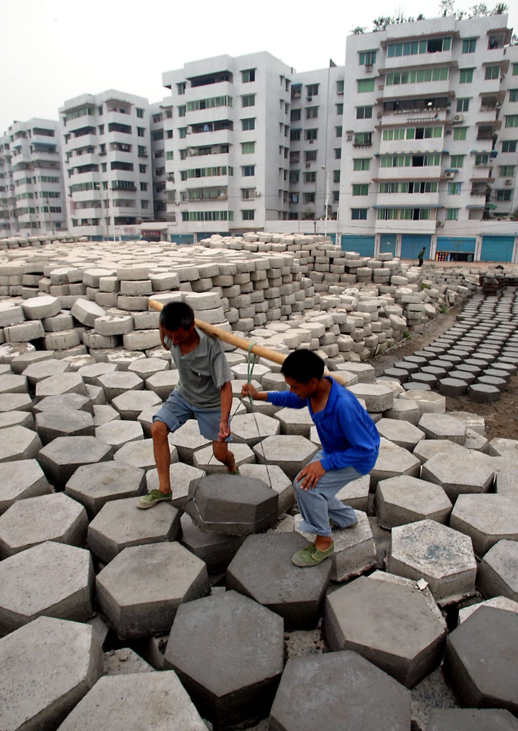 Workers carry the cement slabs which will be laid along the banks of the Yangtze River, to prevent soil erosion at the new Fengdu town with newly built apartments blocks in the background, upriver from the giant Three Gorges dam project, 16 June 2003.