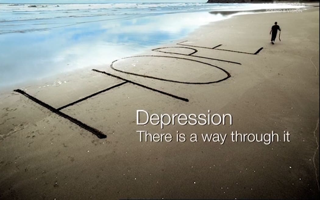 A screenshot from an ad. An aerial view of a beach. The tide is out. "HOPE" is written in big letters on the sand. John Kirwan is walking away in the distance carrying a big stick he used to write the letters. On the right of the screen, in white letters, it reads: "DEPRESSION - THERE IS A WAY THROUGH IT"