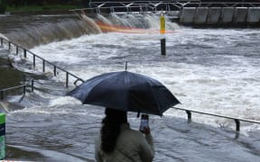 A woman takes pictures of the overflowing Parramatta river at the ferry wharf in Sydney on April 5, 2024, after heavy rain lashed eastern Australia, causing flash flooding and a string of emergency warnings up and down the Pacific coast. (Photo by Saeed KHAN / AFP)