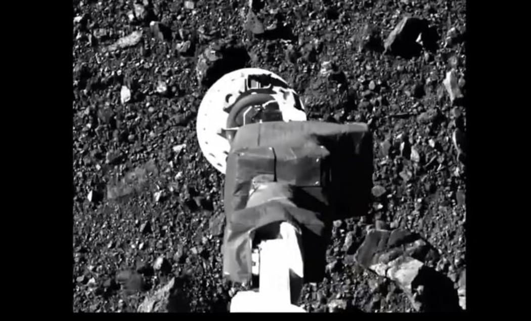 This NASA video frame grab handout image obtained on October 21, 2020 shows NASA's robotic arm from spacecraft Osiris-Rex making contact with asteroid Bennu to collect samples.