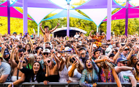 A large crowd of concert goers cheering on an act, with people raising their hands up in the air.