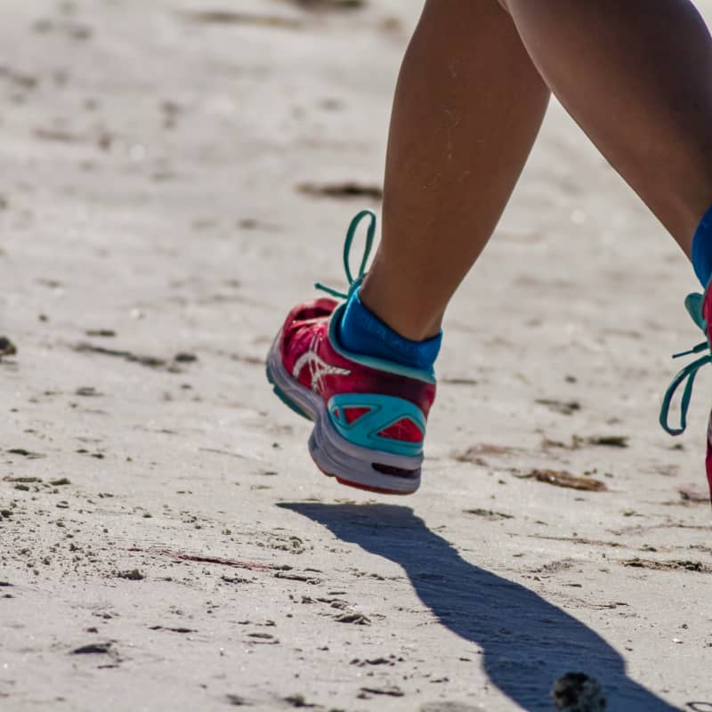 A pair of legs in running shoes move along a beach.