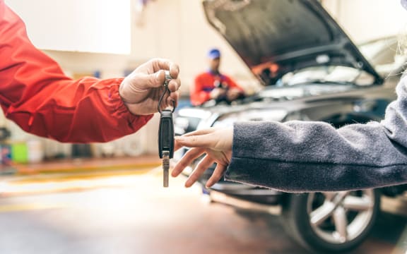 Car workshop, woman picking up her car - Mechanic working on car engine, woman giving automobile key for a check up