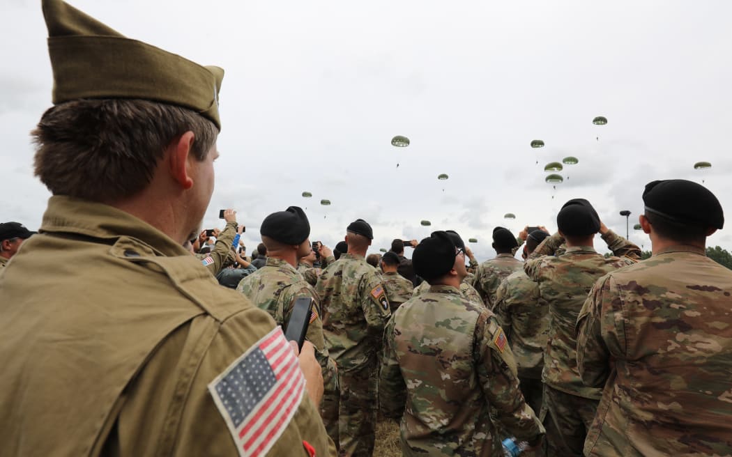 US soldiers and members of the public watch paratroopers taking part in a parachute drop over Carentan, Normandy, north-western France, on 5 June 2019, as part of D-Day commemorations marking the 75th anniversary of the World War II Allied landings in Normandy.