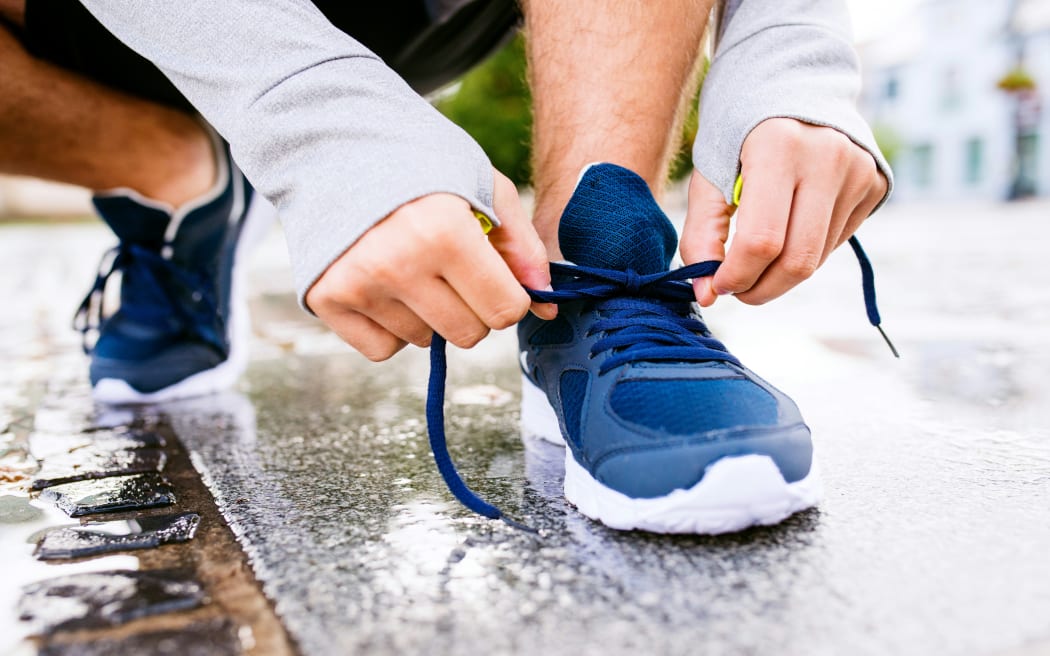 A person crouching on wet outdoors tying their shoe laces.