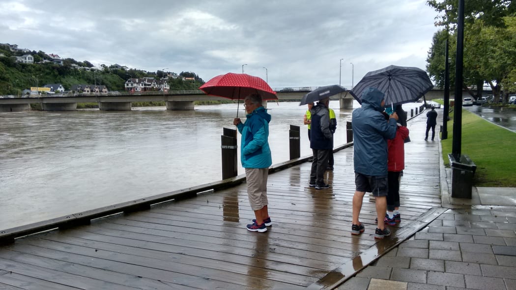 Locals near the town bridge watching logs and other debris from the storm in the headwaters washing down the Whanganui River, ahead of high tide late this afternoon.
