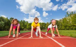 A photo of smiling children on bending knees ready to run a race