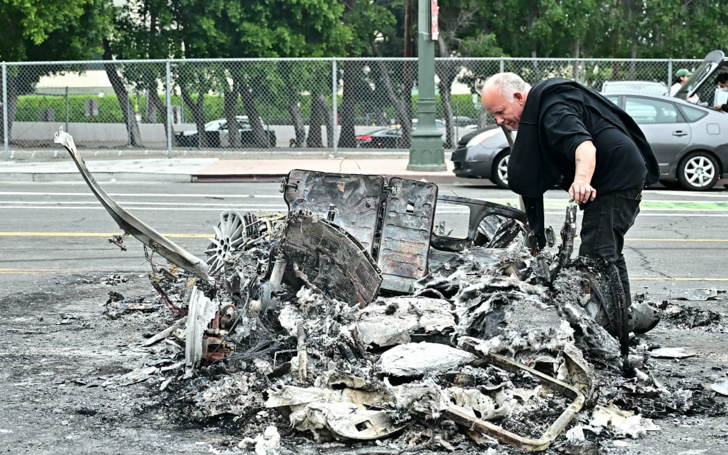 A man looks at the charred remains of a burned Waymo vehicle in the street following a night of protests in response to federal immigration operations in Los Angeles, on June 9, 2025. Los Angeles was on edge Monday after violent clashes between demonstrators and security forces over immigration raids, with the Californian governor vowing to sue President Donald Trump for deploying National Guard soldiers. Police stood watch after ordering people not to gather in the city's downtown where cars were torched over the weekend and security forces fired tear gas at protesters. Protests in Los Angeles, home to a large Latino population, broke out on June 6, triggered by immigration raids that resulted in dozens of arrests of what authorities say are illegal migrants and gang members. (Photo by Frederic J. Brown / AFP)