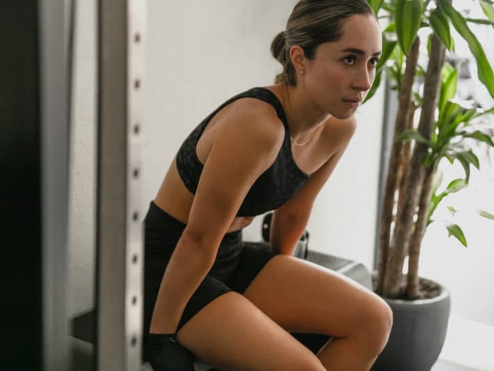 A young woman in workout clothes faces to the side while sitting.