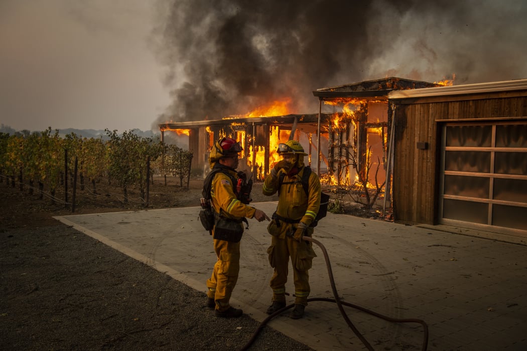 Firefighters discuss how to approach the scene as a home burns near grape vines during the Kincade fire in Healdsburg, California.