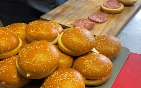 The image shows salami and cheese sandwiches being made using sesame seed burger buns.