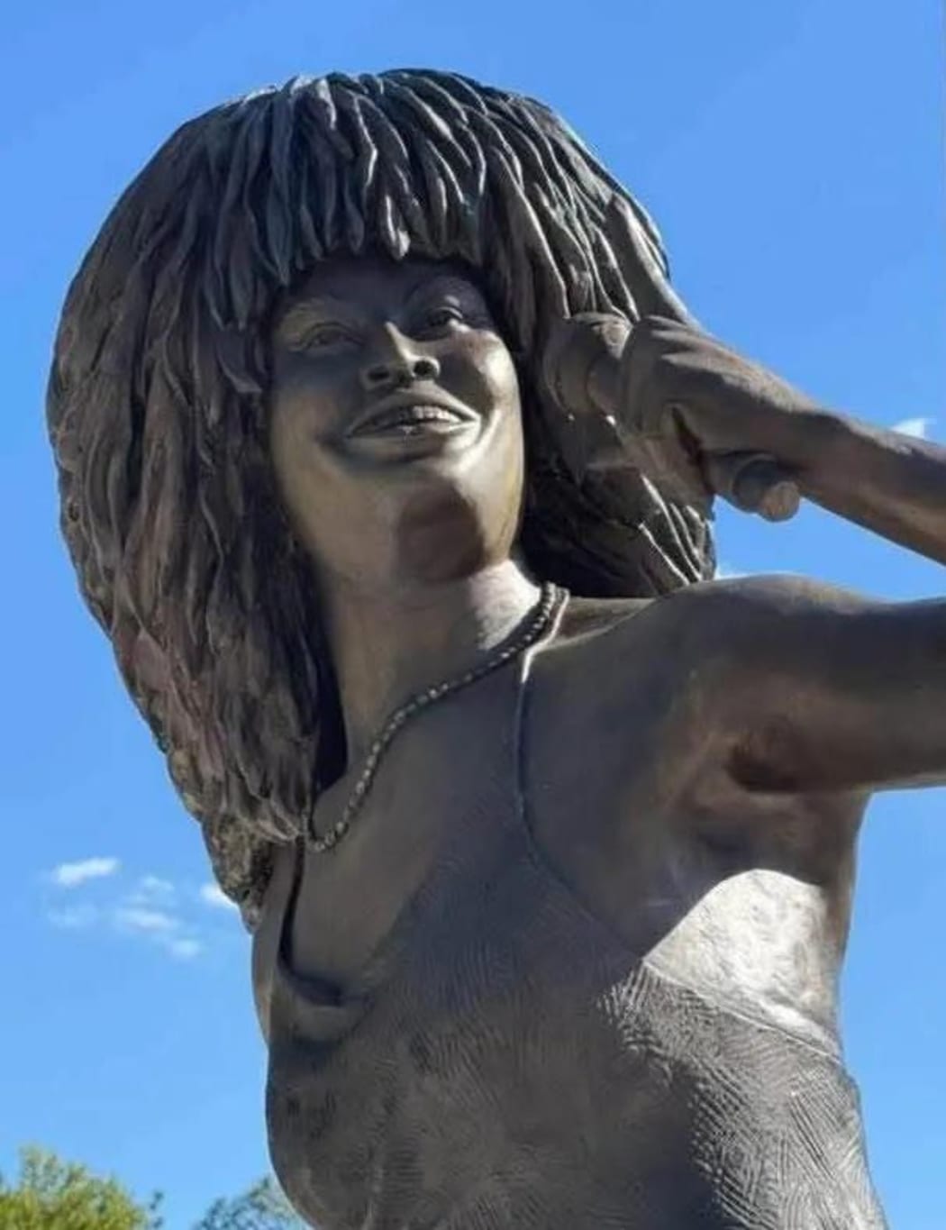A bronze sculpture of Tina Turner smiling and holding a microphone.