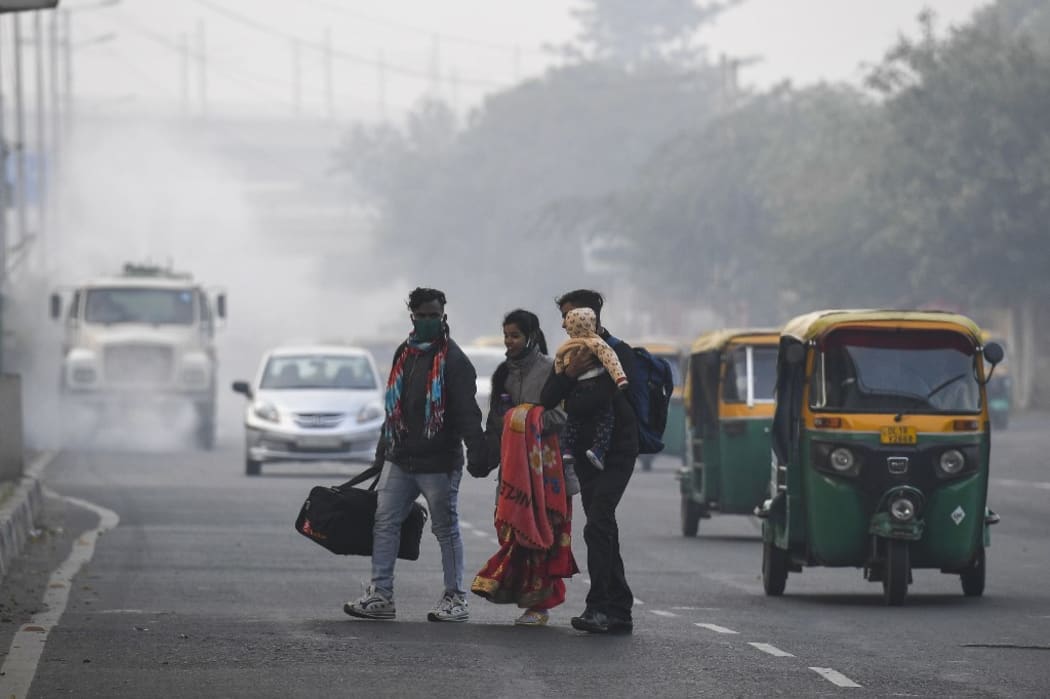 People cross a street as motorists drive past amid smoggy conditions in New Delhi on November 15, 2020. (Photo by Prakash SINGH / AFP)