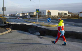 This photo taken on November 13, 2023 shows a member of the emergency services walking near a crack cutting across the main road in Grindavik, southwestern Iceland following earthquakes. The southwestern town of Grindavik -- home to around 4,000 people -- was evacuated in the early hours of November 11 after magma shifting under the Earth's crust caused hundreds of earthquakes in what experts warned could be a precursor to a volcanic eruption.  The seismic activity damaged roads and buildings in the town situated 40 kilometres (25 miles) southwest of the capital Reykjavik, an AFP journalist saw. (Photo by Kjartan TORBJOERNSSON / AFP) / Iceland OUT