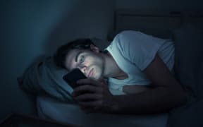 Addicted man chatting and surfing on the Internet with smart phone late at night in bed. Bored, sleepless and tired in dark room with moody light. In insomnia and mobile addiction concept.