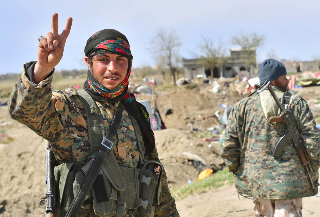 A picture taken on March 23, 2019 shows a fighter of the US-backed Kurdish-led Syrian Democratic Forces (SDF) flashing the V for victory sign in the fallen Islamic State group's last bastion in the eastern Syrian village of Baghuz after defeating the jihadist group.
