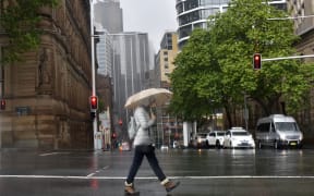 A woman shelters from the rain under an umbrella while crossing a street in Sydney on October 6, 2022. (Photo by Muhammad FAROOQ / AFP)