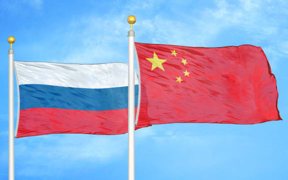 Russia and China two flags on flagpoles and blue cloudy sky background