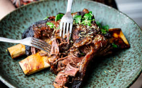 A plate of slow cooked short ribs, being pulled apart by two forks.