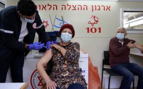 A paramedic administers a dose of the Pfizer/BioNTech coronavirus vaccine to a woman inside a mobile clinic of Magen David Adom at the Mahane Yehuda Market in Jerusalem on February 22, 2021.