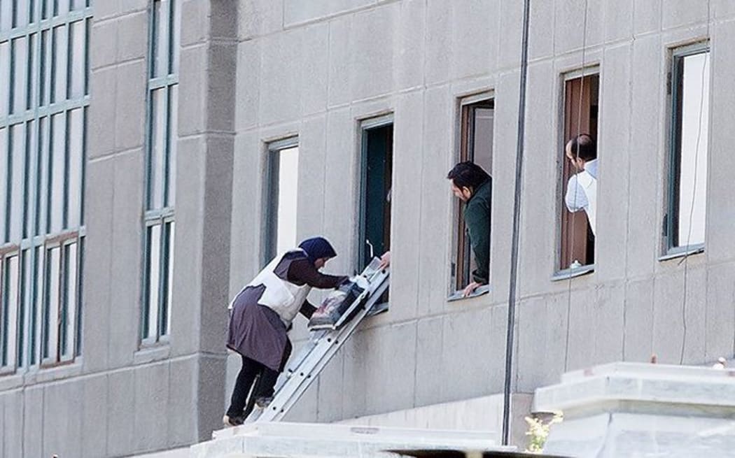 A woman climbs from a window at parliament in Teheran as the building is evacuated during an attack.