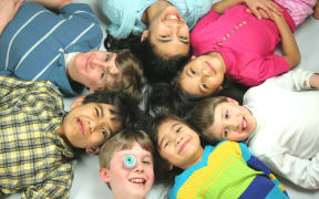 A photo of seven mixed race children all lying with their heads in a circle