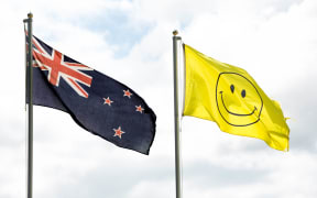 The current New Zealand flag flies alongside a flag with a smiley face on it.