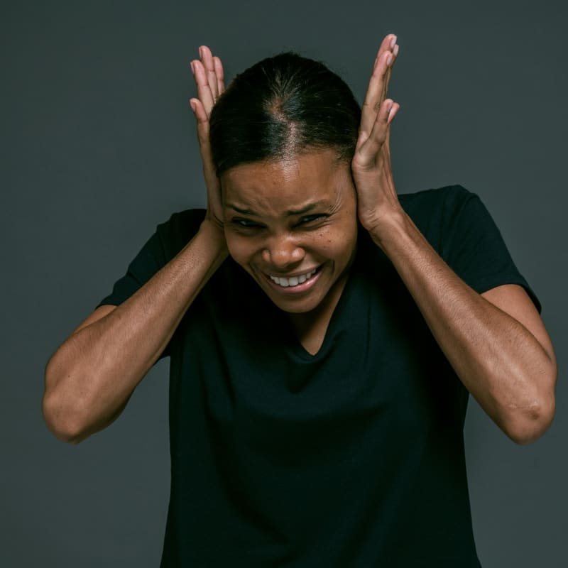 A woman in a black t-shirt covers her ears with her palms.