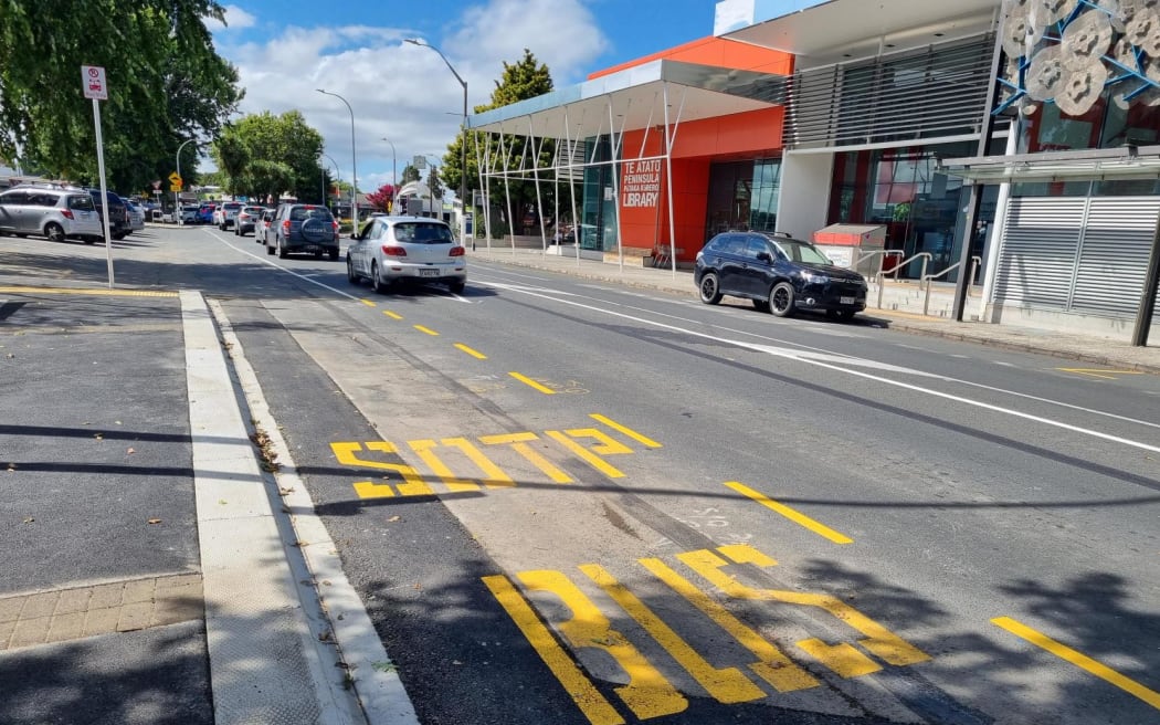 The bright yellow letters painted on Te Atatū Road spell "bus sotp.".