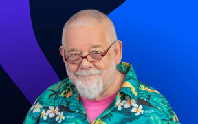 Host William Dart in a bright Hawaiian shirt stands in front of background of abstract shapes in blue and purple on a dark background.