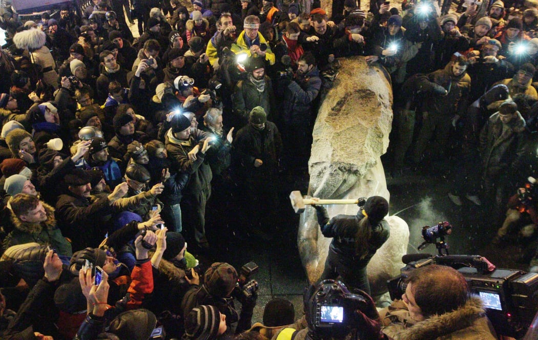 A protester smashes the statue of Lenin.