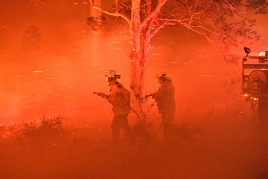 Firefighters struggling against strong winds and flying embers in an effort to secure nearby houses from bushfires near the town of Nowra in the Australian state of New South Wales on 31 December.