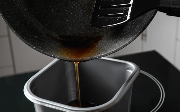 Pouring used cooking oil from frying pan into container, closeup