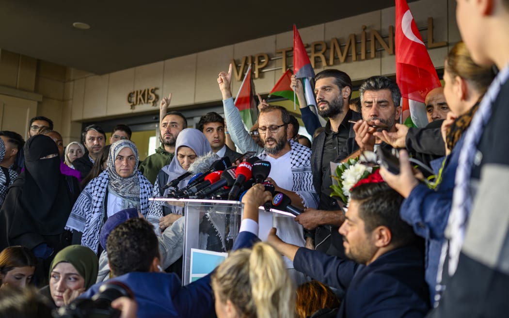 Turkish activist Halil Rifat Canakci (C), one of the activists who were sailing aboard vessels from the Global Sumud Flotilla, speaks to the press after arriving with thirty-six Turks and nationals from 12 countries at Istanbul Airport on a special flight, after Israel stopped a Gaza-bound aid flotilla and detained hundreds of people, in Istanbul on October 4, 2025. "We expect 36 of our nationals on the Global Sumud Flotilla vessels seized by Israeli forces in international waters will return to our country this afternoon via a special flight," Turkish foreign ministry spokesman Oncu Keceli said on X, adding that the number has not been finalised. The Turkish diplomatic source said nationals from the United States, United Arab Emirates, Algeria, Morocco, Italy, Kuwait, Libya, Malaysia, Mauritania, Switzerland, Tunisia, and Jordan planned to be on the Turkish Airlines flight. (Photo by Yasin AKGUL / AFP)