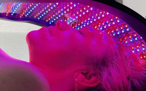 Close up of Stacey Morrison, host of Healthy or Hoax, lying under a Celluma light therapy device with red and blue lights on her face.
