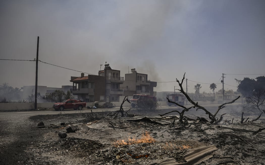 This photograph taken on July 24, 2023, shows firefighting vehicles parked outside houses amid a fire between the villages of Kiotari and Genadi, on the Greek island of Rhodes. Firefighters tackled blazes that erupted in peak tourism season, sparking the country's largest-ever wildfire evacuation -- and leaving flights and holidays cancelled. Tens of thousands of people have already fled blazes on the island of Rhodes, with many frightened tourists scrambling to get home on evacuation flights. (Photo by Spyros BAKALIS / AFP)