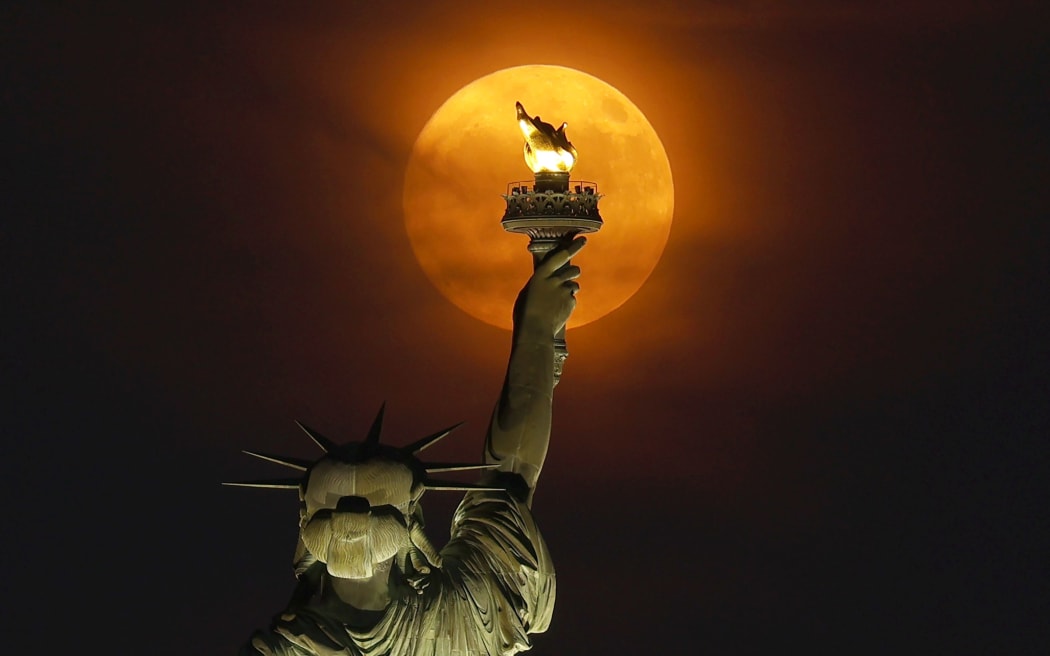 JERSEY CITY, NJ - JULY 2: A 99.7 percent illuminated Buck Moon rises through a haze behind the Statue of Liberty in New York City on July 2, 2023, as seen from Jersey City, New Jersey.  (Photo by Gary Hershorn/Getty Images)