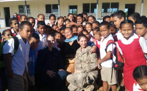 The photo shows Lieutenant Diana Denhaan from the Royal New Zealand Nursing Corps and Leading Aircraftman Chantelle Ramage with school children from Government Primary School Tongoleleka.