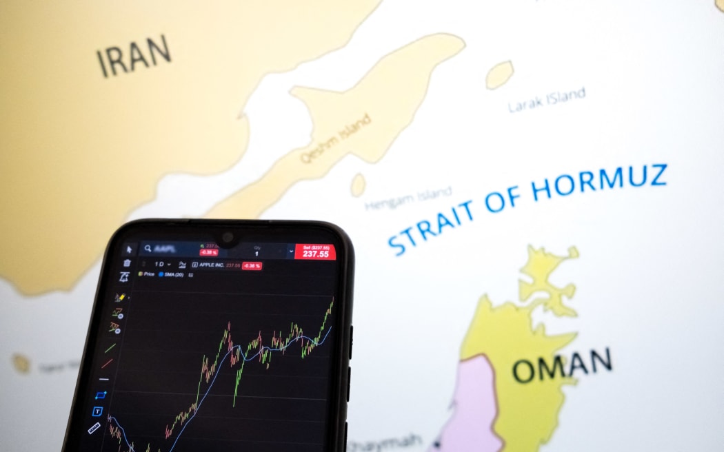 A stock exchange curve appears on a smartphone screen, and a map shows the Strait of Hormuz on a laptop computer screen in this photo illustration taken in Athens, Greece, on March 3, 2026. (Photo by Nikolas Kokovlis/NurPhoto) (Photo by Nikolas Kokovlis / NurPhoto via AFP)