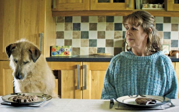 Film still from the movie Róise and Frank showing Frank the dog and Róise sitting together at the dinner table.