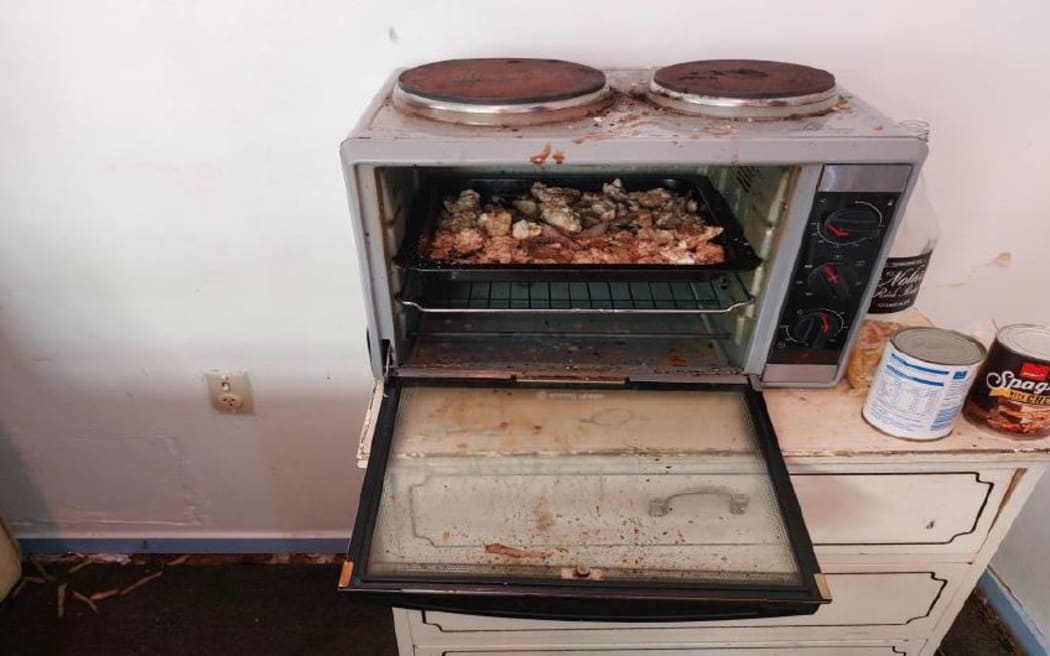 An image from the Spa Lodge report of a mini kitchen bench-top oven in a room with food remaining.