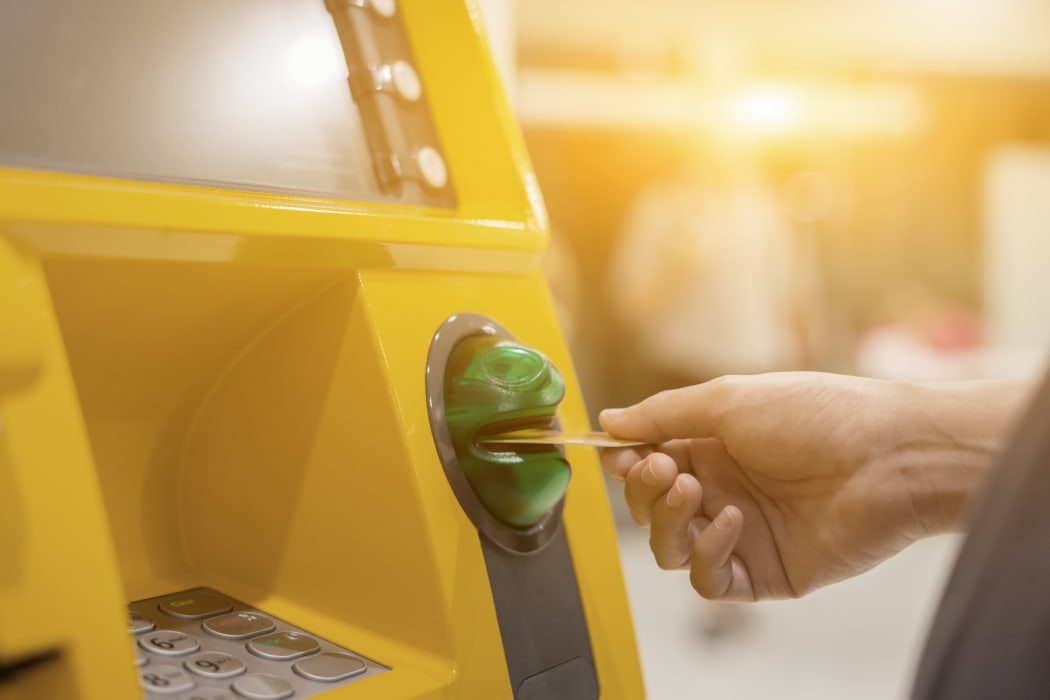 Person inserting bank card into ATM machine to withdraw money.