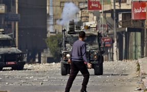 A Palestinian youth holds a rock as he faces an Israeli military vehicle, during a raid on the occupied-West Bank city of Nablus, on 22 February 2023.