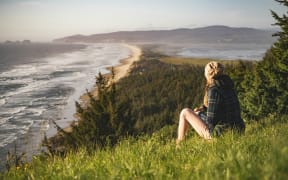 Person sitting on a grassy hill overlooking a coastline.