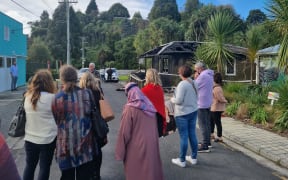 People stand around in the street outside the building as a press conference is given.